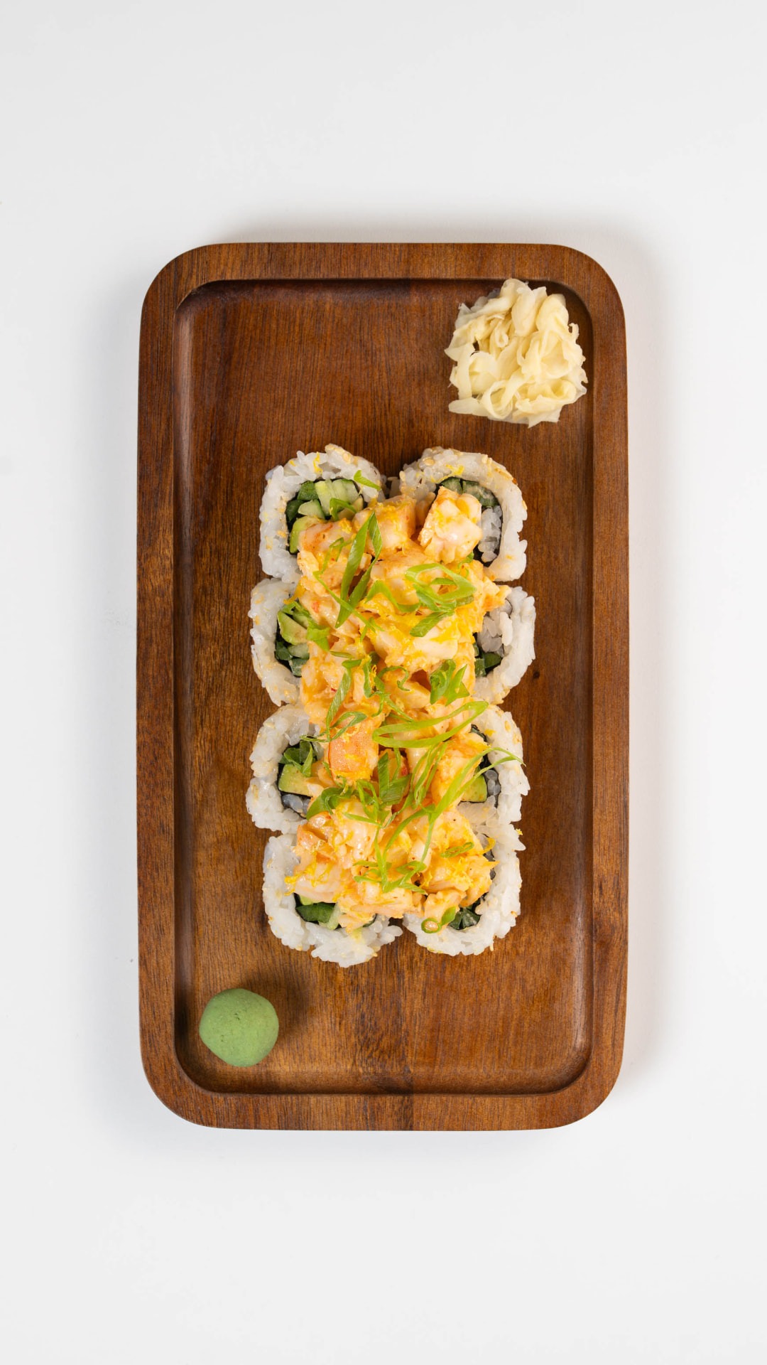 Spicy Shrimp Roll topped with shrimp salad and scallions on a wooden board