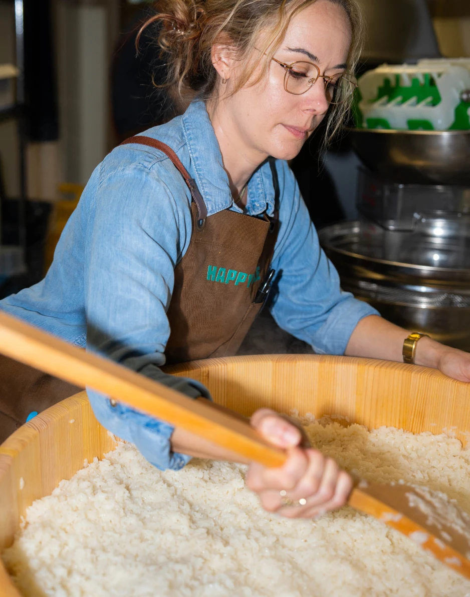 Happy Rice team member mixing sushi rice in a large wooden tub