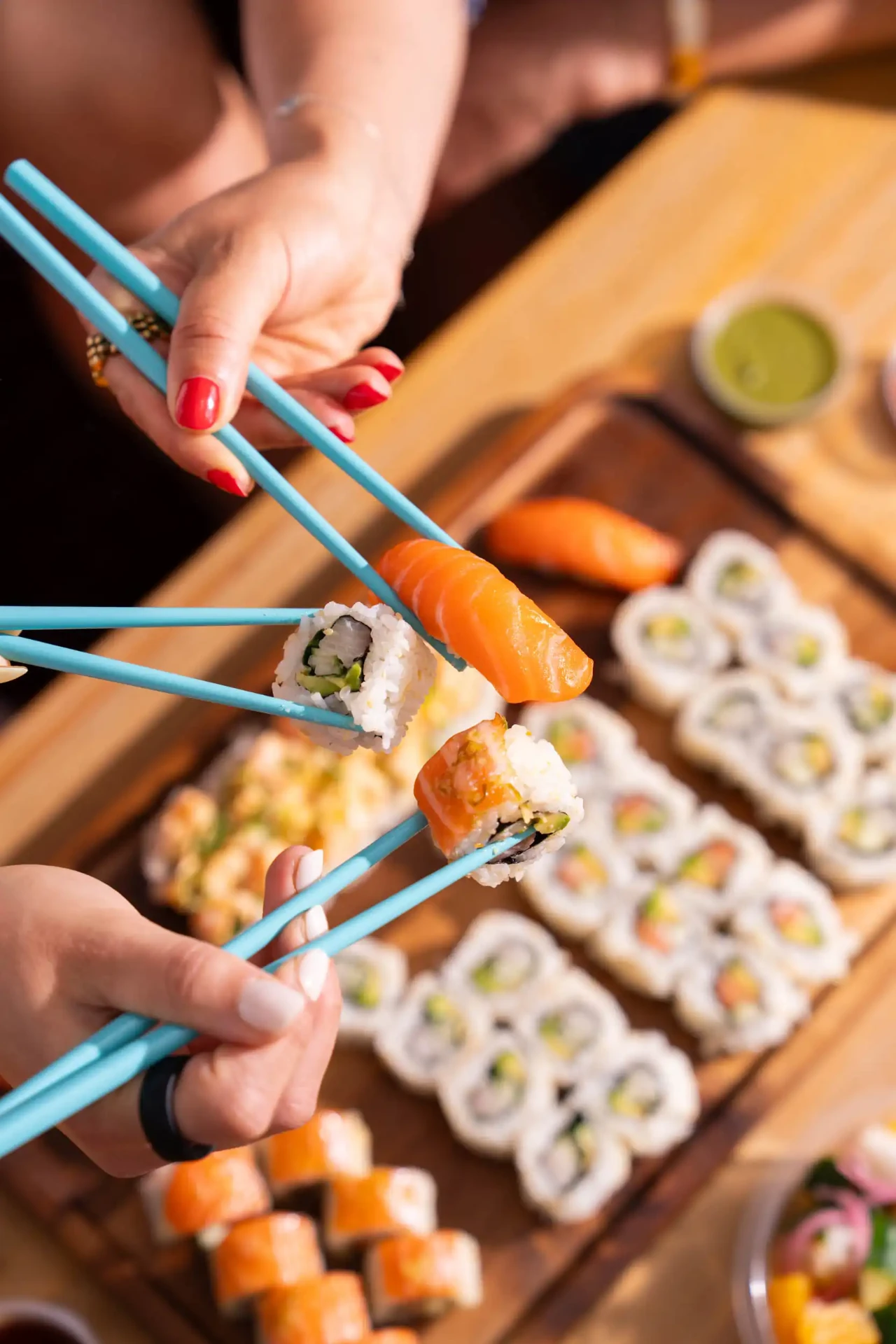 Friends sharing Happy Rice nigiri and rolls with teal chopsticks over a sushi platter