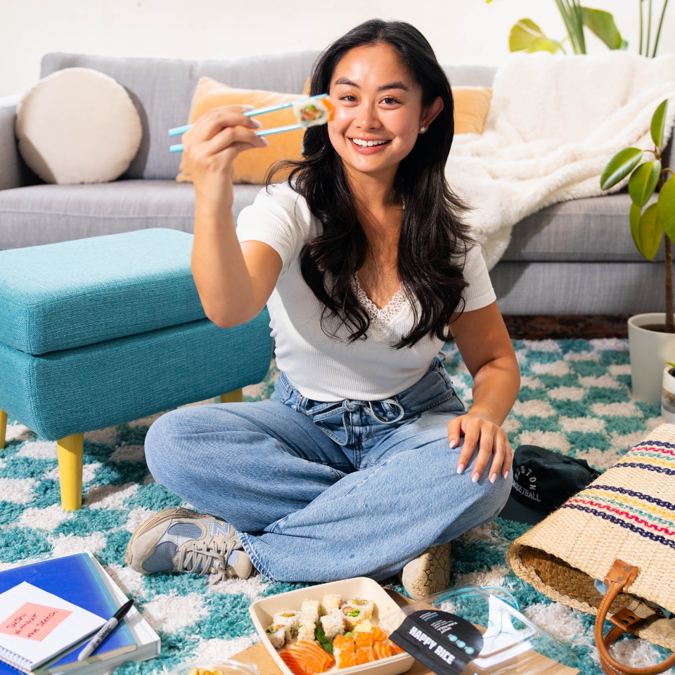 Woman at home eating Happy Rice sushi with teal chopsticks