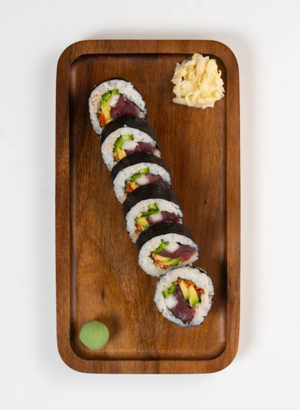 Deluxe Spicy Tuna Roll sliced on a wooden board with pickled ginger and wasabi