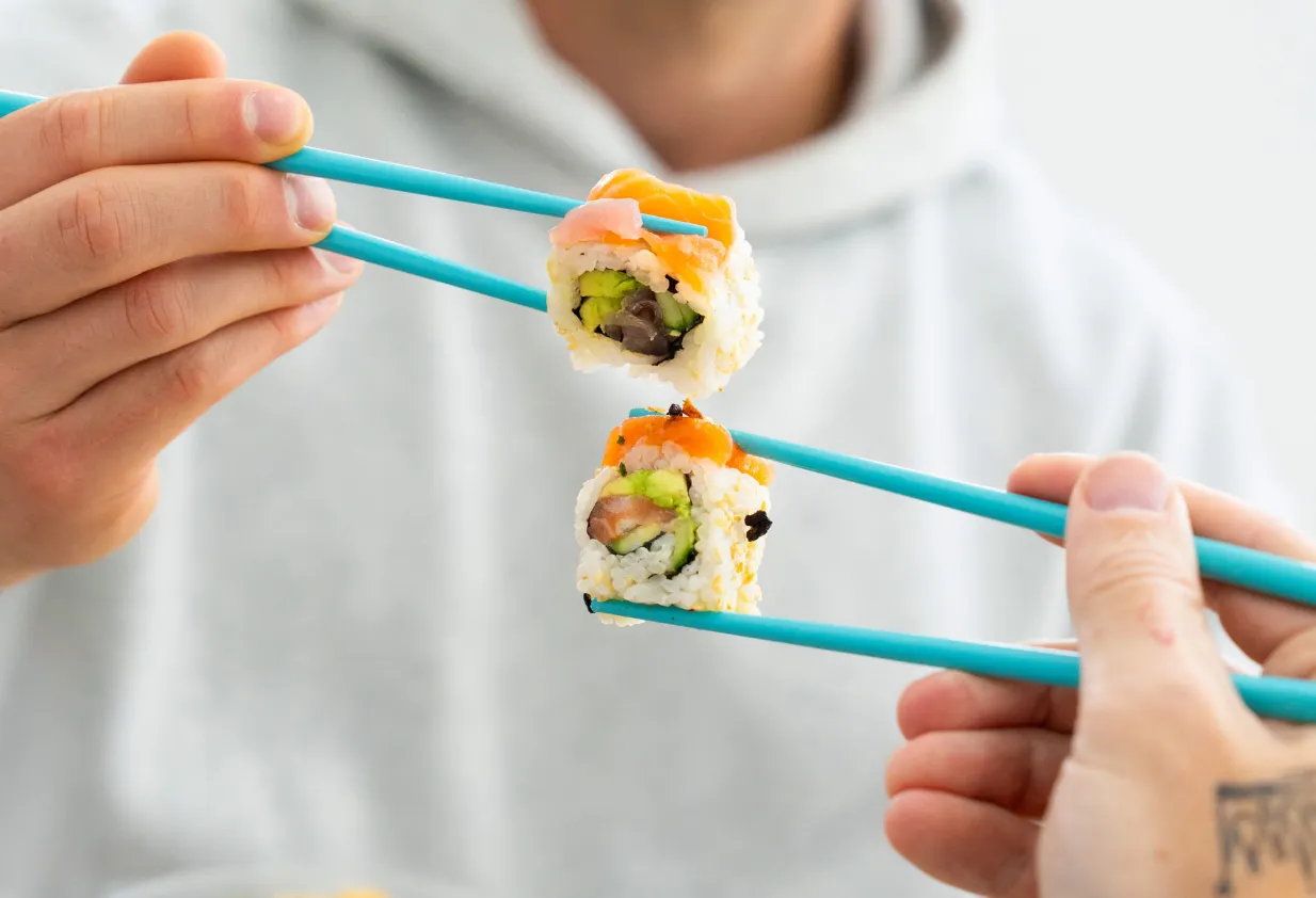 Two Happy Rice sushi rolls held up with teal chopsticks