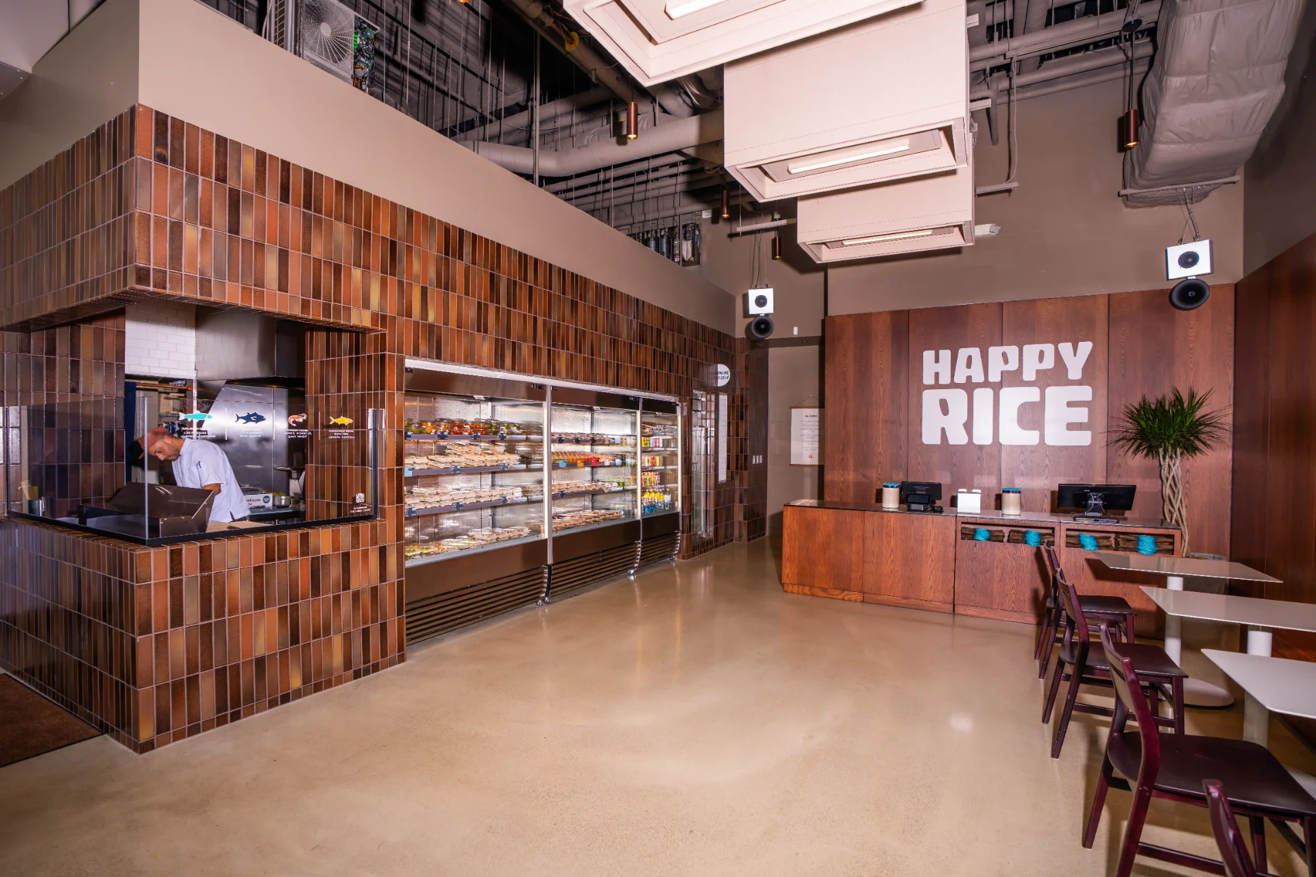 Inside Happy Rice Boston Seaport at 53 Boston Wharf Road: tiled sushi bar, grab-and-go cases and HAPPY RICE wall sign